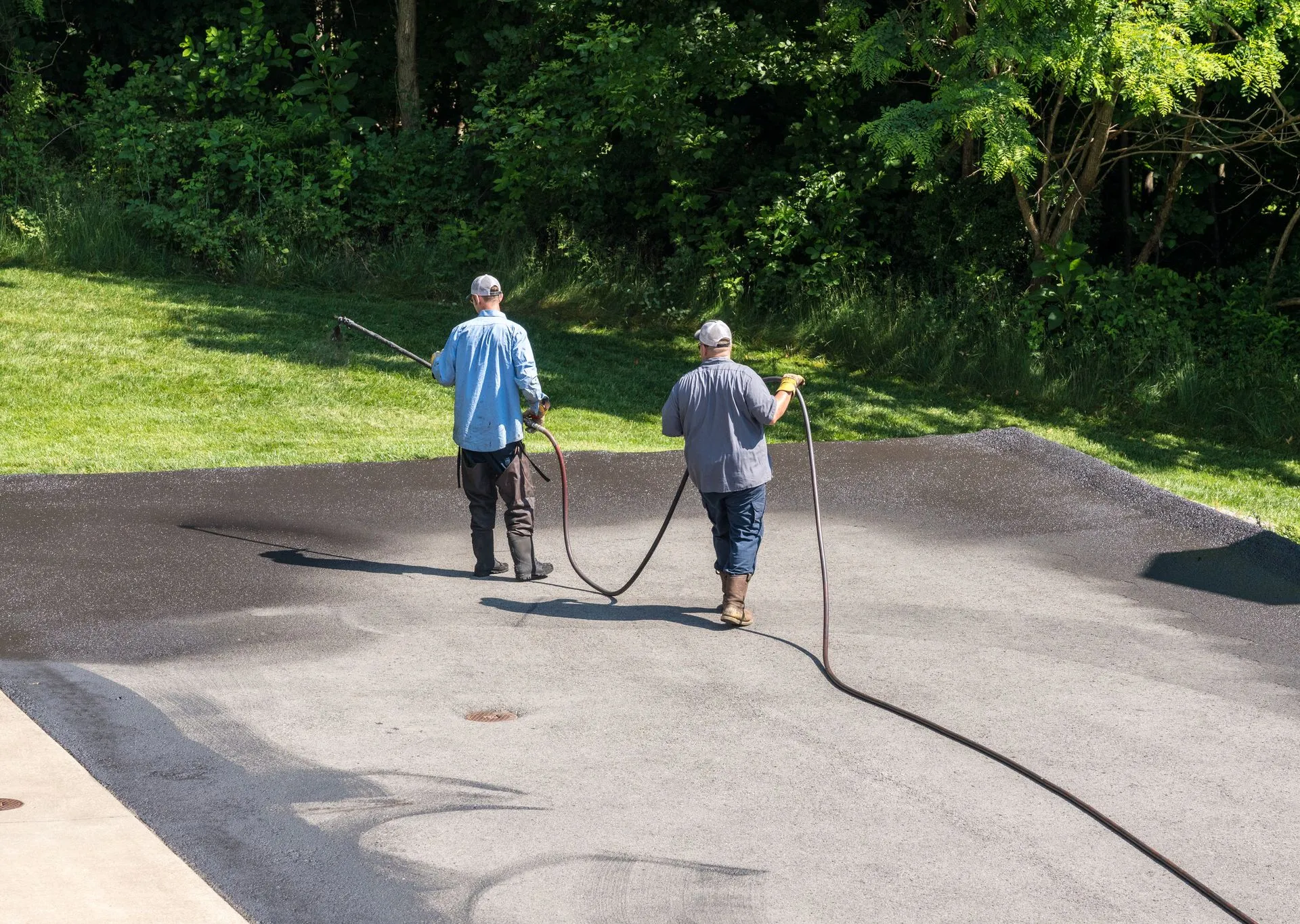 asphalt+driveway+installation+trinity+nc-1920w Workers sealing a driveway with hoses.